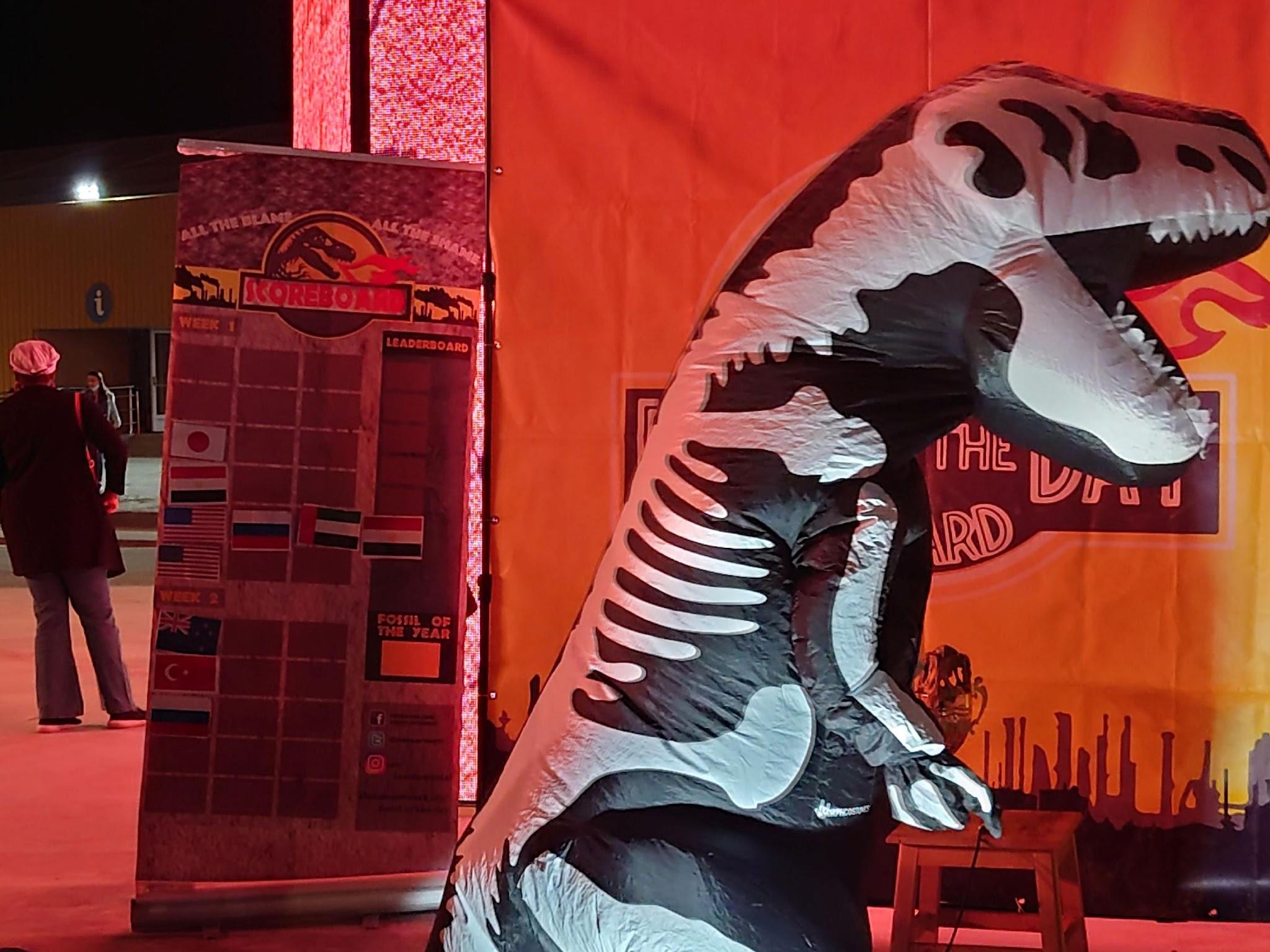 写真）“Five minutes to showtime“と書いたメモを観客に見せて回る化石賞のマスコットである恐竜。主催者自ら言う通り、ショータイムなのだ。