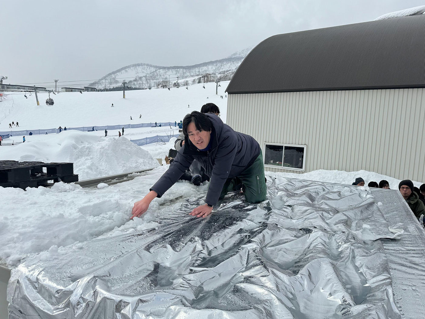 写真）融雪実験用のプレハブの屋根の上でデモンストレーションする電気通信大学榎木光治准教授（2024年1月18日　北海道ニセコにて）